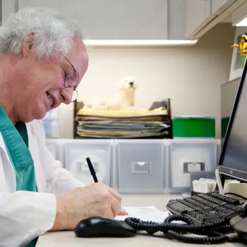 Dr. Franklin of Oregon Veterinary Specialty Hospital smiling while writing at his desk 